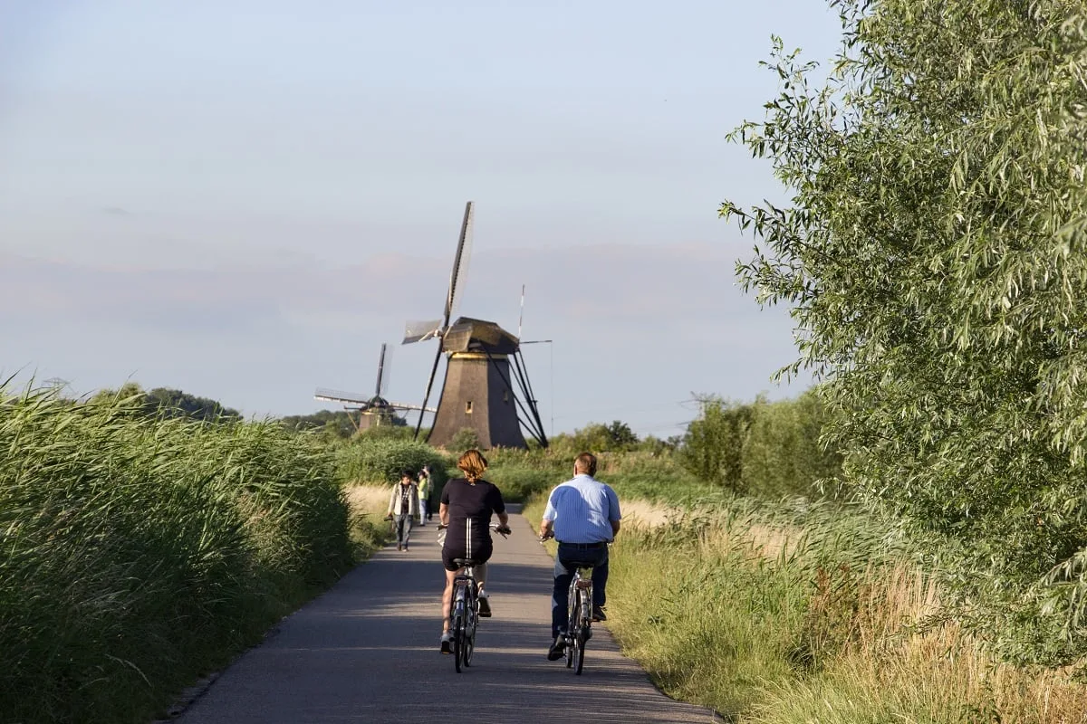 Cyclistes sur un chemin dans la verdure, avec un moulin au fond