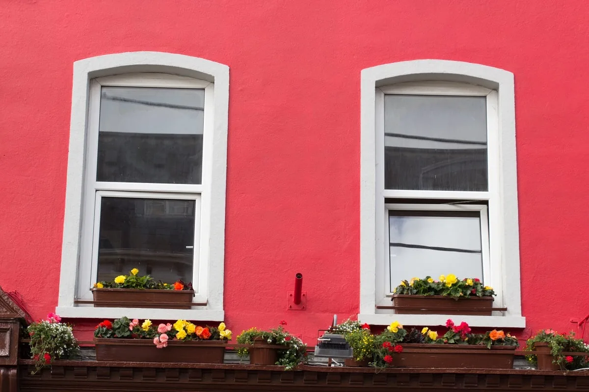 Façade d'une maison en rouge avec deux fenêtres et des bacs à fleur