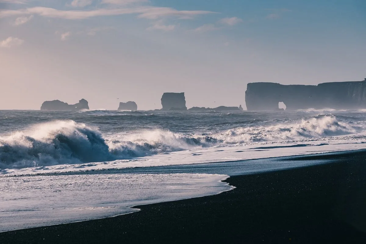 Le cap de Dyrhólaey au loin, avec une mer agitée au premier plan