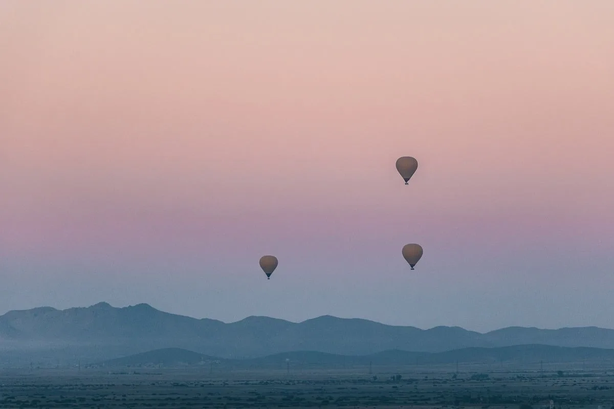 Lever de soleil avec les montagnes au fond et 3 montgolfières dans le ciel