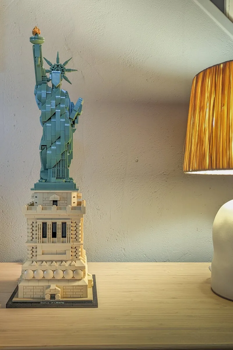 La statue de la Liberté Lego exposée sur un meuble avec une lampe allumée à côté
