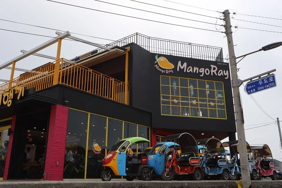 Café MangoRay aux façades noires avec des tuk-tuks colorés garés devant