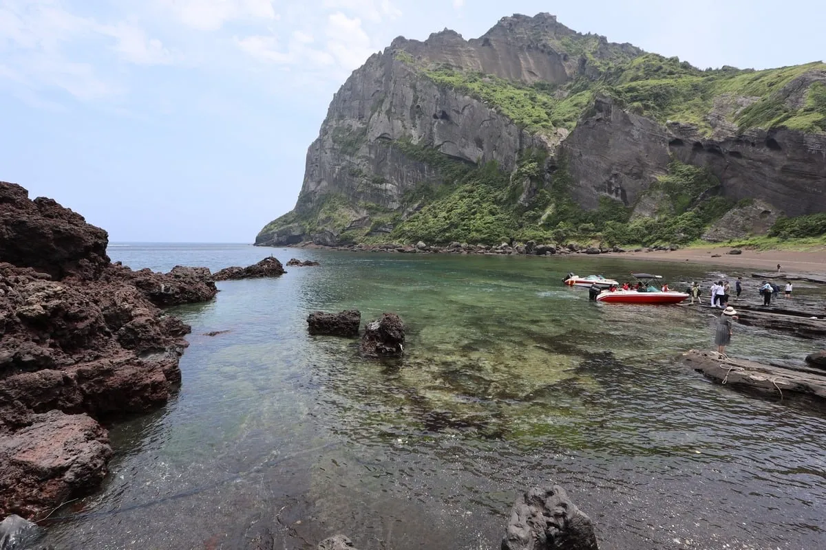 Crique rocheuse volcanique avec bateaux et falaise verdoyante en arrière-plan