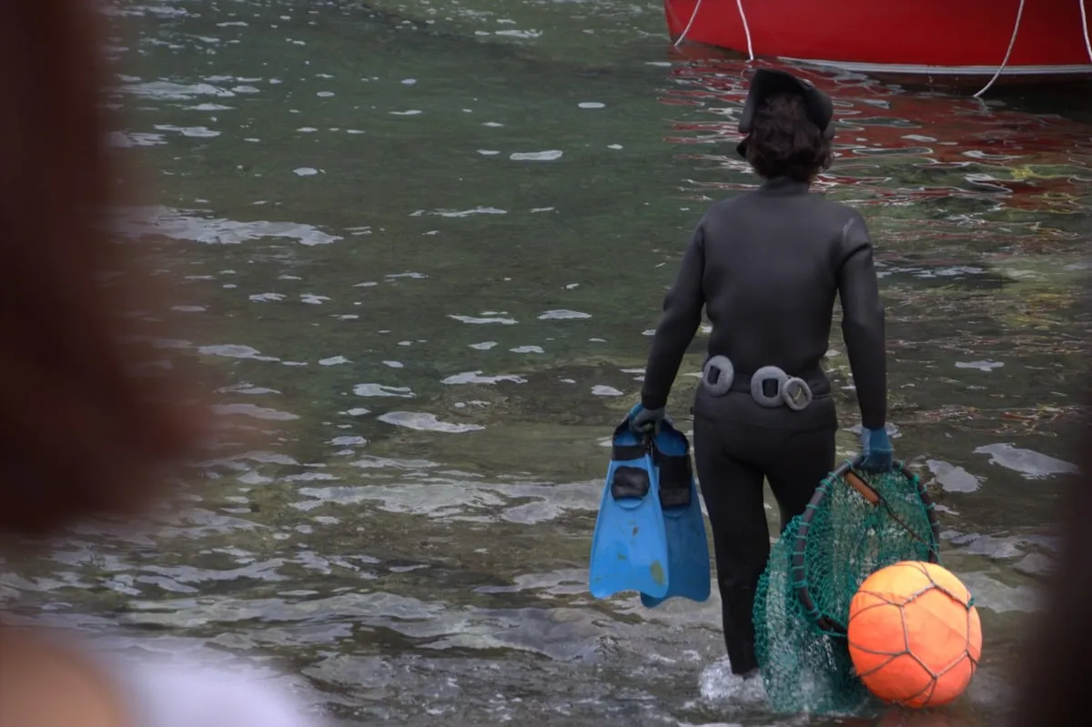 Plongeuse en combinaison noire portant palmes bleues et filet de pêche