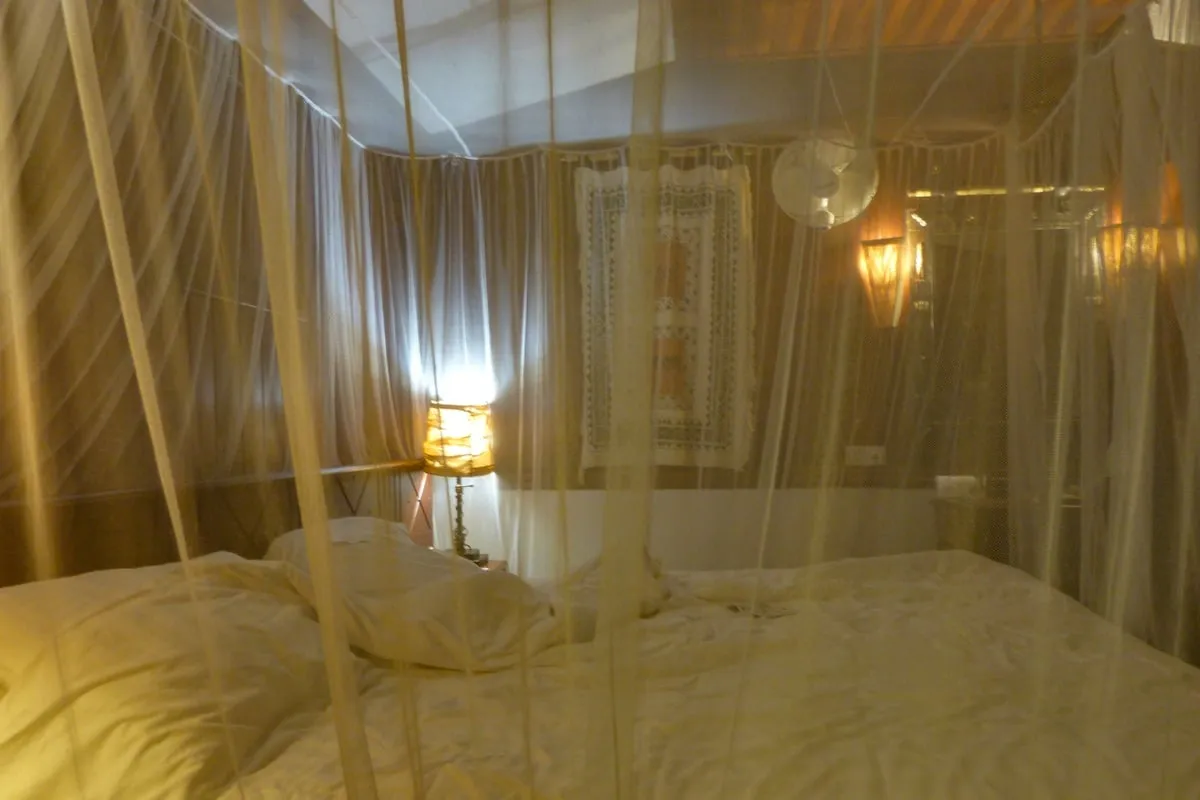 Chambre avec lit double entouré d'une moustiquaire et lampe allumée