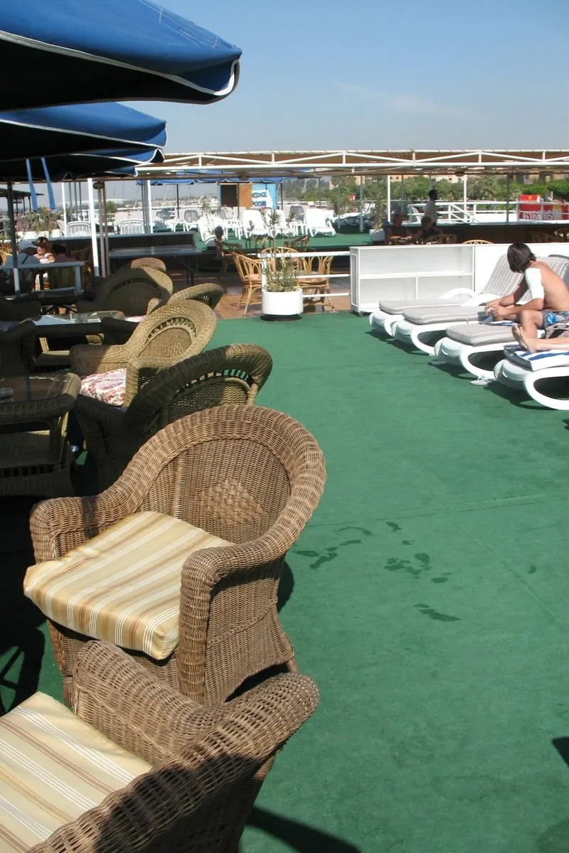 Fauteuils en rotin sur terrasse verte avec parasols bleus en arrière-plan