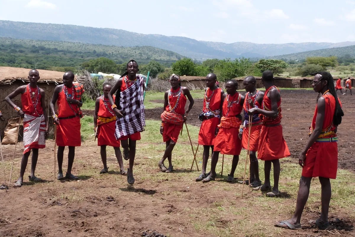 Groupe d'hommes Maasai en tenue rouge traditionnelle dont l'un saute en l'air