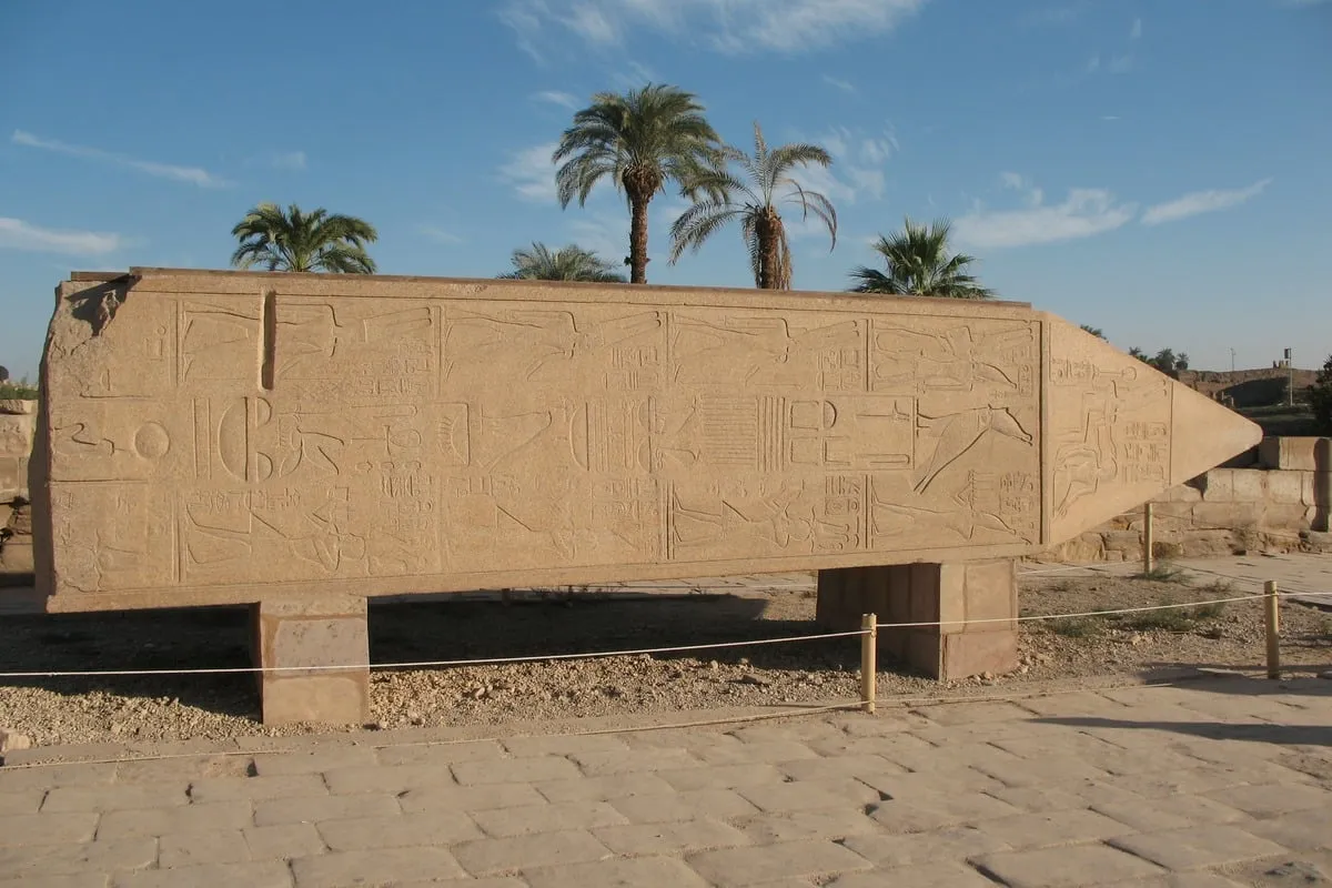 Obélisque couché en grès avec hiéroglyphes gravés et palmiers en arrière-plan