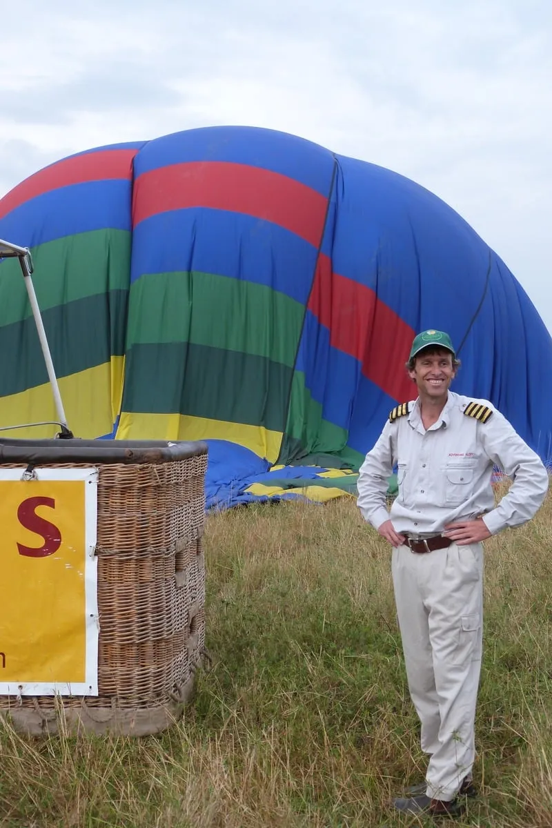 Pilote en uniforme souriant devant une montgolfière au sol